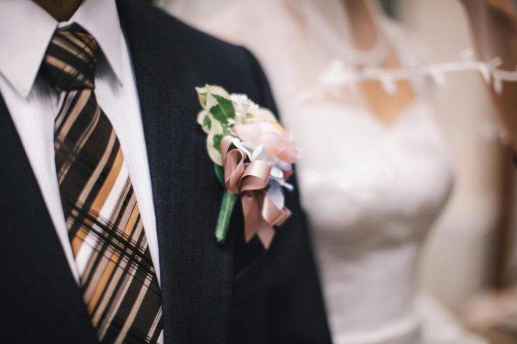 Groom in dark suit with boutonniere and bride in white wedding dress in background